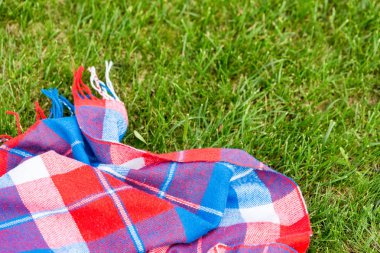 Taze ot çimenlikte damalı parlak battaniye. Canlı kırmızı, yeşil ve mavi renkler. Üstten görünüm. Boşaltmak