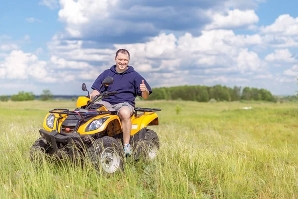 Mann, der auf einem Quad in einer wunderschönen Naturlandschaft fährt. Fahrer zeigt Daumen hoch Zeichen. landschaftliche Wiesen und Felder Landschaft. Reise und Abenteuer concep — Stockfoto