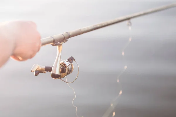 Fishing at sunrise. Close-up fisherman hand with spinning fishing rod. Summer morning on river or lake. Copyspace.