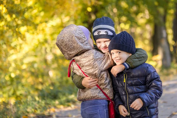 Group of happy three kids having fun outdoors in autumn park. Cute children enjoy hugging together against golden fall background. Best frend forever and happy childhood concept.