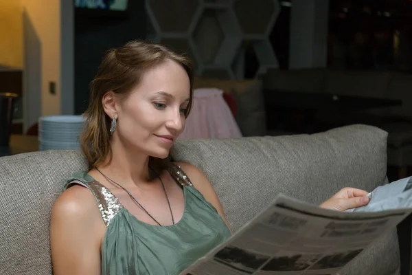 Akşam restoranda oturan ve menü veya gazete okuma elbiseli Genç güzel zarif kadın. Çekici beyaz kız kanepe kafede dinlendirici