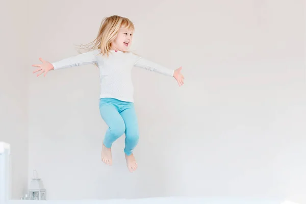 Happy kid jumping over bed. Cute little blond girl having fun indoors. Happy and careless childhood concept — Stock Photo, Image