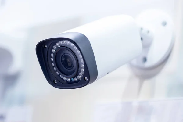 Big white professional surveillance camera. CCTV mounted on ceiling. LED IR lights around lens. Security system concept. Copyspace, neutral light blue backgound.
