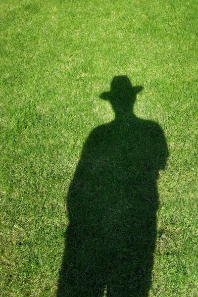 Shadow silhouette of man wearing hat on green grass lawn. Human shade on fresh natural meadow.