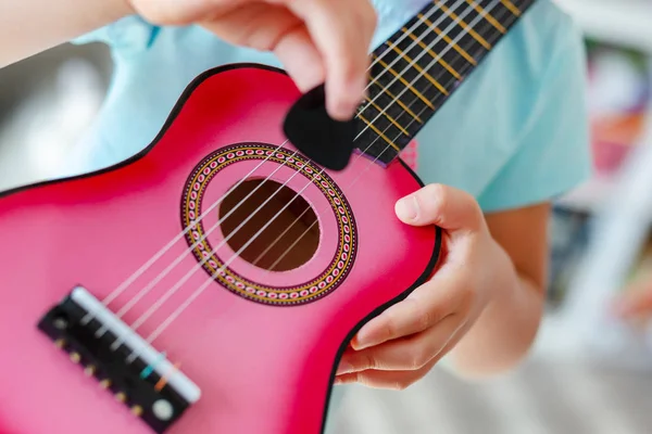 Close-up pequeña linda chica rubia que se divierte aprendiendo a tocar la pequeña guitarra ukelele en casa. niña tratando de jugar juguete instrumento musical en el interior —  Fotos de Stock