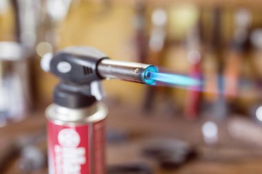 Gas cartridge gun lighter .Close-up nozzle of burner with blue flame jet. Workshop background, scorching of wood clipart