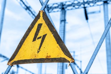 Yüksek gerilim uyarı işareti ile eski yaşlı paslı üçgen metal plaka. Transformatörler ve elektrik dağıtım hatları ile güç istasyonu. Dışarıda tutmak