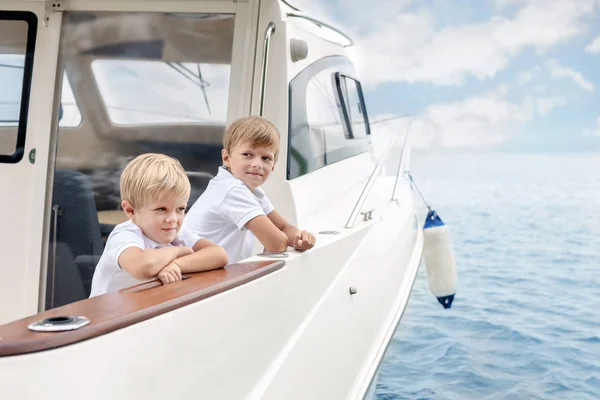 Dois meninos loiros caucasianos bonitos a bordo de iate de luxo branco no dia de verão brilhante. Irmãos se divertindo aprendendo iatismo tohether. Viagem e aventura com conceito de crianças — Fotografia de Stock