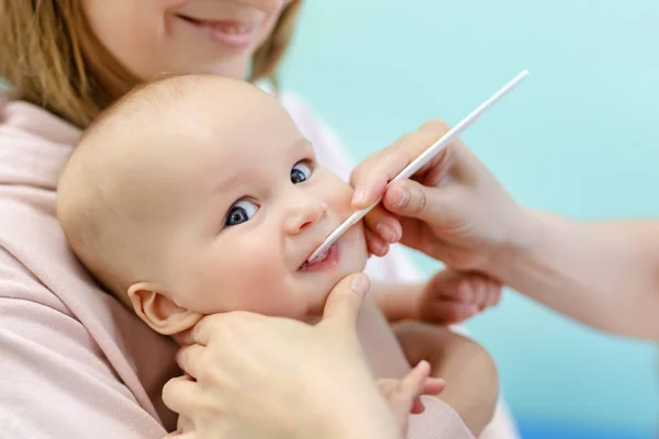 医師のオフィスで母親の手の赤ちゃん 小児科医は 舌圧子で少しかわいい幼い少年の喉の検査を行います 歯が生える期間 子供たちの医療や病気予防のコンセプト — ストック写真