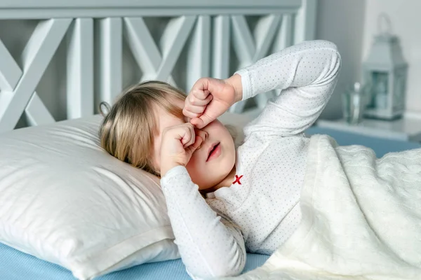 Cute little blond caucasian girl awakening at bed in morning. Child wake up early to go to school. Stretching and yawning. Healthy sleeping. Children healthcare — Stock Photo, Image