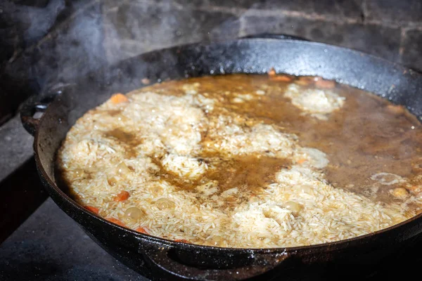 Cozimento Arroz para mandíbula ou paella em caldeirão de ferro sobre fogo aberto. Fumaça e vapor. Comida saborosa preparando fundo processo ao ar livre — Fotografia de Stock