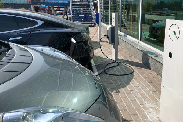 Зарядка электромобиля с подключенным кабелем питания на электромобильной зарядной станции. Эко-электромашина припарковалась у современного офисного здания со стеклянным фасадом
.