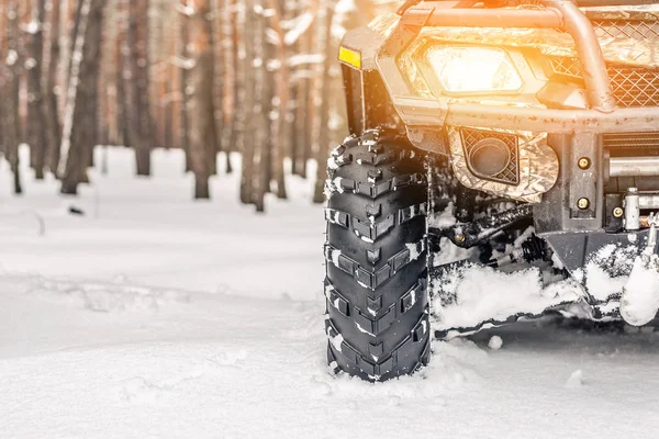 Close-up ATV 4wd quad bike in forest at winter. 4wd all-terreain vehicle stand in heavy snow with deep wheel track. Seasonal extreme sport adventure and trip. Copyspace.