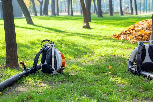 Ciężkich dmuchawa do liści leżącego na czyste trawa w parku miejskim w jesieni. Sezonowe pozostawia usługi czyszczenia i usuwania jesienią — Zdjęcie stockowe