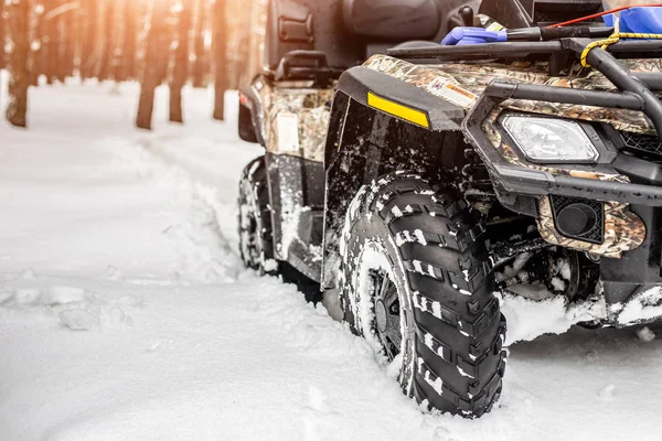 Close-up ATV 4wd quad bike in forest at winter. 4wd all-terreain vehicle stand in heavy snow with deep wheel track. Seasonal extreme sport adventure and trip. Copyspace.