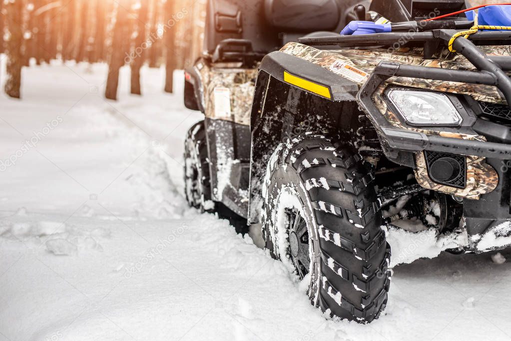 Close-up ATV 4wd quad bike in forest at winter. 4wd all-terreain vehicle stand in heavy snow with deep wheel track. Seasonal extreme sport adventure and trip. Copyspace.