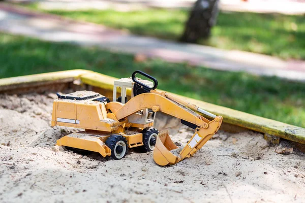 Juguete de excavadora amarillo en caja de arena de madera en el patio. concepto de juguetes para niños — Foto de Stock