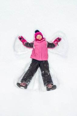Cute little kid girl in warm ski sport suit making snow angel outdoors. Kid having fun lying on snowdrift after snow storm in winter. Children outdoor activities. Winter vacation and holidays. clipart