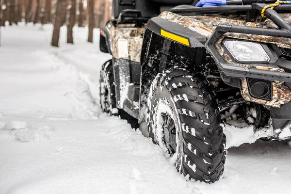 Close-up ATV 4wd quad bike in forest at winter. 4wd all-terreain vehicle stand in heavy snow with deep wheel track. Seasonal extreme sport adventure and trip. Copyspace.