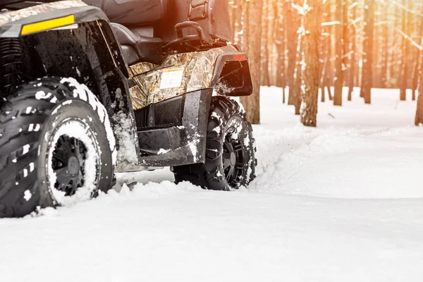 Close-up ATV 4wd quad bike in forest at winter. 4wd all-terreain vehicle stand in heavy snow with deep wheel track. Seasonal extreme sport adventure and trip. Copyspace.