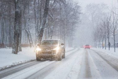 Kışın akşam saatlerinde yoğun kar yağışında şehir caddesinde kaygan yolda giden arabalar. Kar fırtınası ve kar fırtınası yüzünden trafik tıkanıklığı. Hava tahminleri.