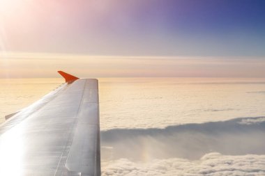 Şafakta bulutlar üzerinde uçan bir uçak. Uçak kanadı üzerinde dramatik renkli günbatımı ve gündoğumu sırasında güzel cennet. Seyahat ve tatil kavramı.