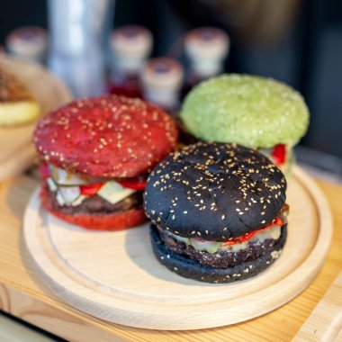 Üç lezzetli parlak renkli sığır eti burgers gıda fest ahşap kasada. amburger topuz clolred ile domates, fesleğen ve mürekkep balığı mürekkep