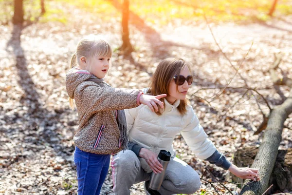 Fiatal felnőtt anya és a kislányom gyaloglás együtt az erdőben vagy parkban, a ragyogó napsütéses napon. Aranyos szőke kislány mutató ujjával valahol — Stock Fotó