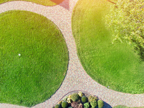 Aerial drone view of backyard garden with circle wath path, green grass lawn and trees. Landscape design and gardening