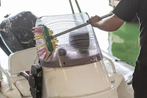 Homem que lava o barco inflável branco com escova e sistema de água de pressão na garagem. Serviço de bordo e conceito de manutenção sazonal — Fotografia de Stock