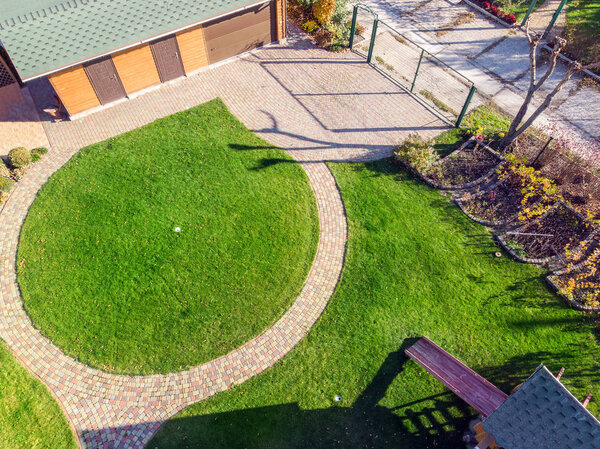 Aerial drone view of backyard garden with circle wath path, green grass lawn and trees. Landscape design and gardening