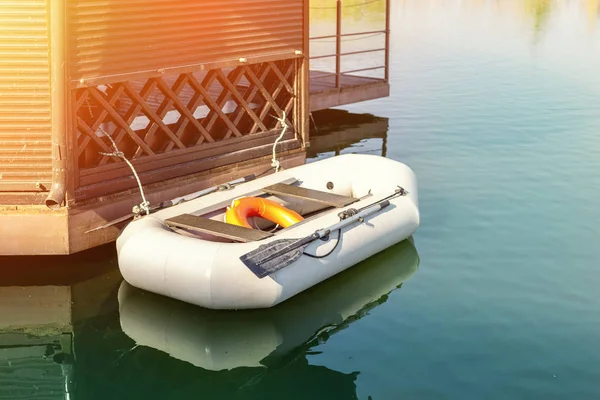 Kleine opblaasbare roeiboot met peddels afgemeerd in de buurt van de houten prieel op pier. Vissersboot vastgebonden op de oever van het meer of rivier vroeg zonsopgang tijdig — Stockfoto