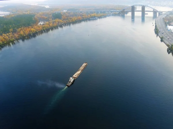 Paisagem aérea panorâmica de Kiev e do rio Dnipro ao pôr do sol. Barca de apoio rebocador com materiais a granel de areia a descer o rio Dnieper. Navegação interior ucraniana e carga fluvial — Fotografia de Stock