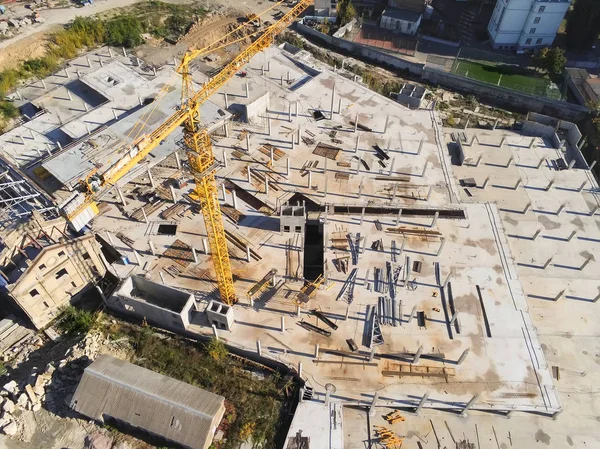 Construction site aerial view. Mall building base with solid concrete pillars. Heavy machinery and high tower crane working. Industrial aerial background