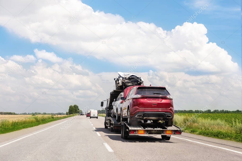 Tow truck trailer on highway carrying three damaged cars sold on insurance car auctions for repair and recovery.  Vehicles shipment and rescue service