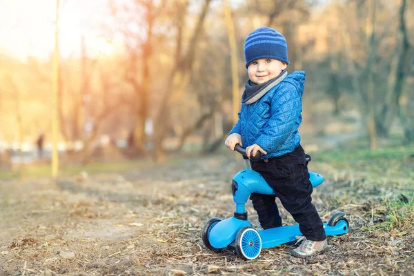 Aranyos imádnivaló kaukázusi kisgyermek fiú a kék kabát szórakozik lovaglás háromkerekű mérleg fuss kerékpár robogó a városi parkban vagy erdőben. Szabadtéri sporttevékenységek gyerekeknek — Stock Fotó