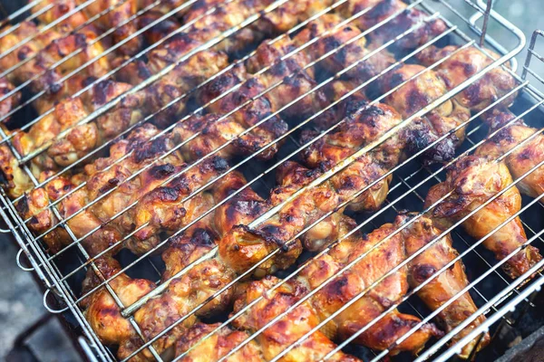 Κοντινό-πάνω φτερούγες κοτόπουλου που μαγειρεύουν σε μεταλλικό πλέγμα μπάρμπεκιου σε σχάρα. Υπαίθριο πάρτι το Σαββατοκύριακο στην αυλή. Νόστιμο χρυσό καφέ νόστιμο γεύμα μπάρμπεκιου — Φωτογραφία Αρχείου