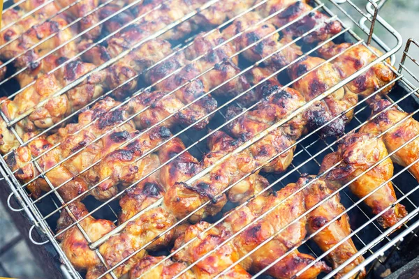 Κοντινό-πάνω φτερούγες κοτόπουλου που μαγειρεύουν σε μεταλλικό πλέγμα μπάρμπεκιου σε σχάρα. Υπαίθριο πάρτι το Σαββατοκύριακο στην αυλή. Νόστιμο χρυσό καφέ νόστιμο γεύμα μπάρμπεκιου — Φωτογραφία Αρχείου