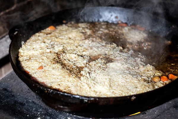 Rijst koken voor pilaw of paella in ijzer ketel boven open vuur. Rook en stoom. Lekker eten bereiden buiten proces achtergrond — Stockfoto