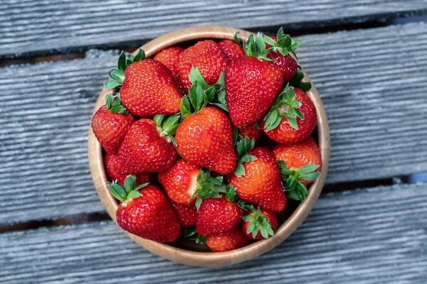 Sweet fresh juicy organic ripe strawberries in wooden bowl on wooden surface outdoors