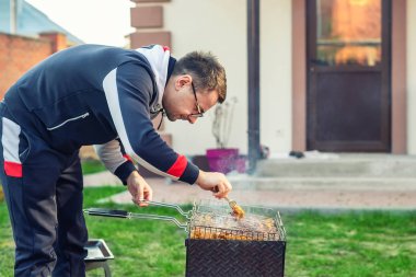 Erkek kişi açık ateş brazier ızgara tavuk kanatları hazırlanıyor. Barbekü evin arka bahçesinde ev partisi friens. Weeken bbq aile öğle yemeği