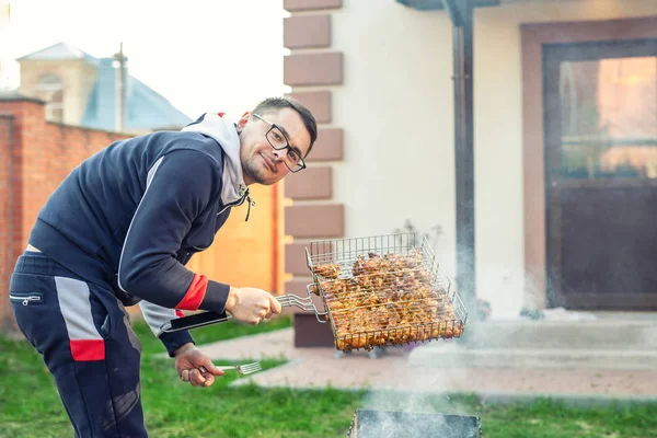 Мужчина готовит куриные крылышки на гриле в жаровне. Вечеринка друзей барбекю на заднем дворе дома. Weeken барбекю семейный обед — стоковое фото