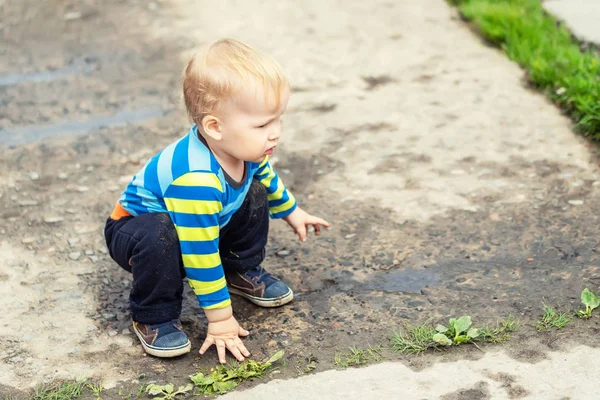 Χαριτωμένο μικρό λευκό ξανθό νήπιο αγόρι που έχει τη διασκέδαση κείτεται σε μια λακκούβα μετά τη βροχή σε εξωτερικούς χώρους. Περίεργο παιδί ανακαλύπτει τον κόσμο στη λάσπη — Φωτογραφία Αρχείου