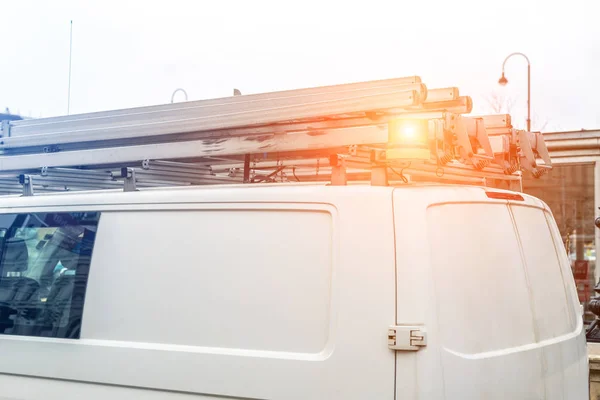 Белый ремонтно-сервисный фургон с лестницей и оранжевым фонарем на крыше на улице города. Автомобиль команды поддержки или монтажа — стоковое фото