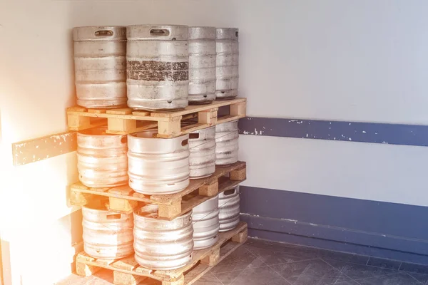 Used metal beer keg barrel on wooden pallets in corner of warehouse after delivery. Steel drink containers storage — Stock Photo, Image