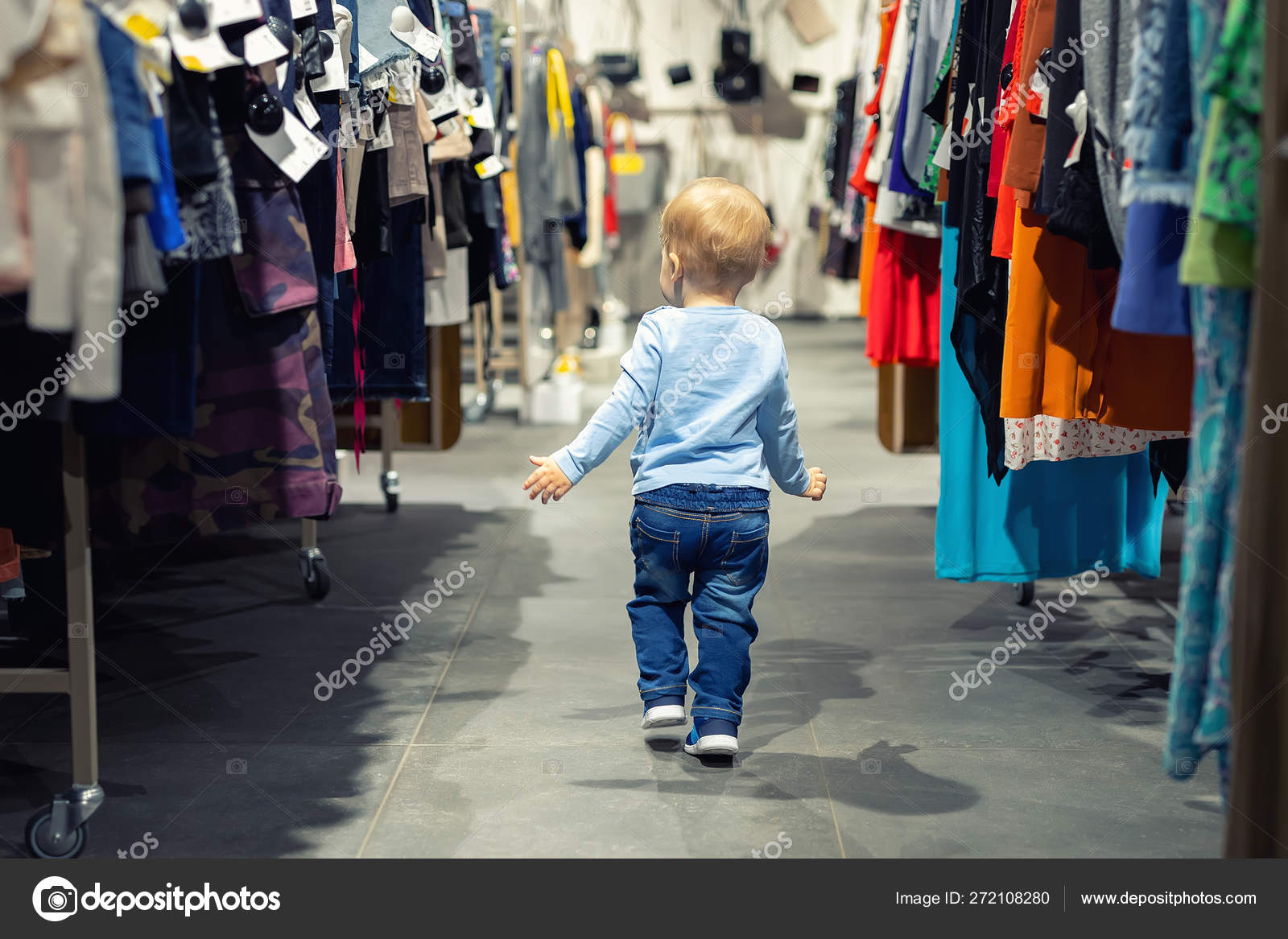 Cute caucasian blond toddler boy walking alone at clothes retail