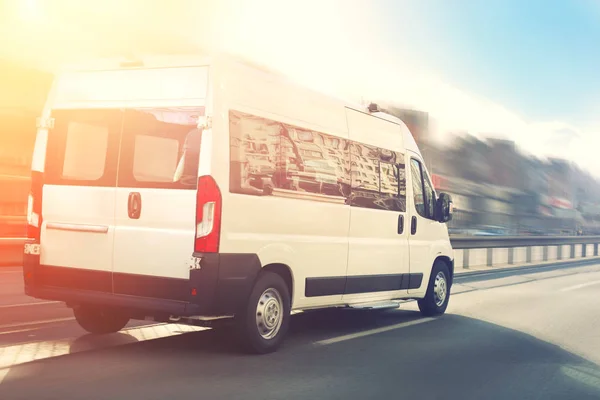 Onherkenbaar klein passagiers busje schiet op de snelweg bij City Street Traffic met stedelijk stadsgezicht en zonsondergang hemel op achtergrond. Charter of shuttlebus van haast op weg met bewegingsonscherpte effect — Stockfoto