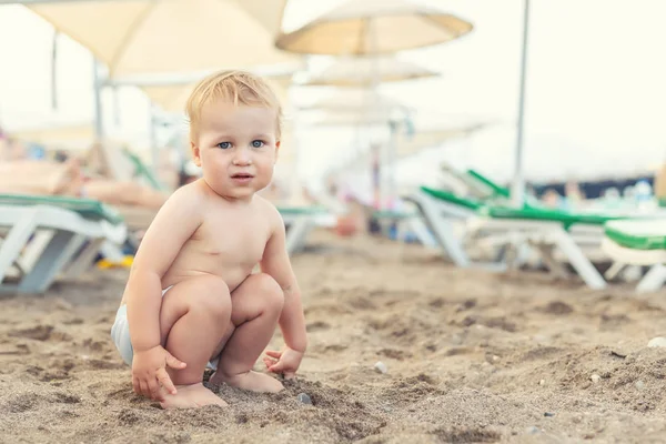 Sevimli kafkas toodler çocuk şezlong arasında kumlu plajda tek başına çömelme. Tatil gezisi sırasında sahil kıyısında oynarken eğlenen sevimli mutlu çocuk