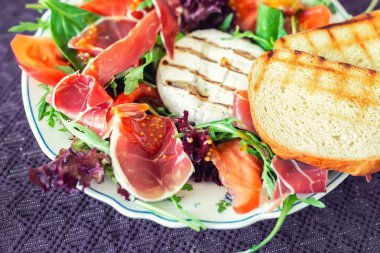 Izgara camembert peyniri, prosciutto jambon, organik domates ve taze yeşil yaprakları ile lezzetli karışık salata yemeği. Sağlıklı özenli yemek. Siyah üzerinde izole