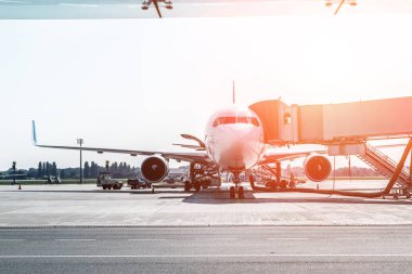 Havaalanı üzerinde büyük modern ticari uçak gün doğumu veya gün batımında biniş köprüsü ile demirledi. Arka planda mavi berrak gökyüzü. Seyahat ve turistik destinasyon konsepti